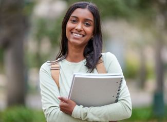 Female student of color holding notebooks lookign at camera