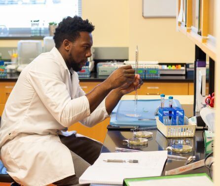 Student in a lab coat handles a serological pipette